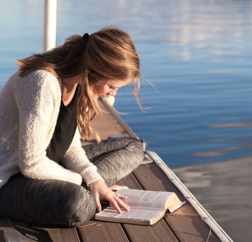 Girl reading a book on a dock